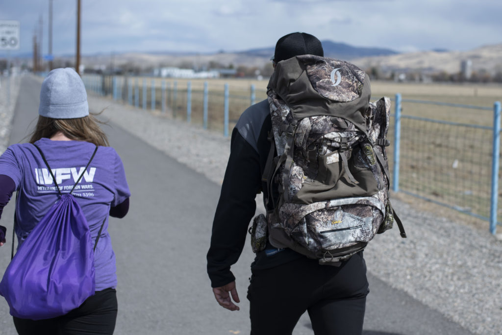 Un hombre y una mujer con mochilas, caminando por un sendero al lado del camino.