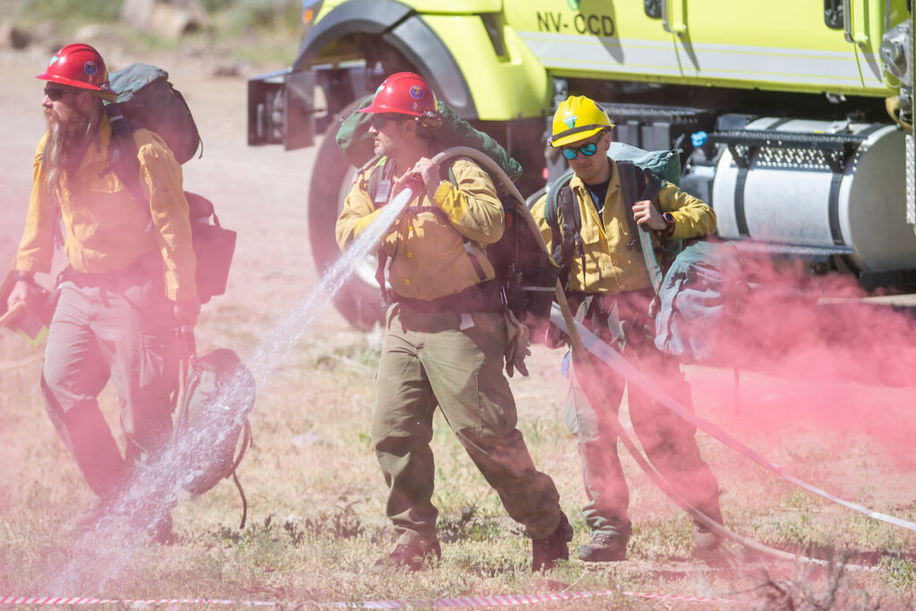 Los bomberos son fotos con una manguera activa en primer plano y el camión al fondo