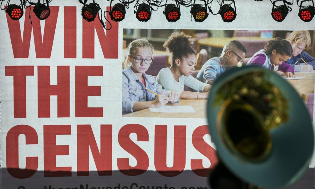 Foto de otra imagen que dice "ganar el censo" en inglés e incluye niños. Frente a la imagen se puede ver una trompeta.