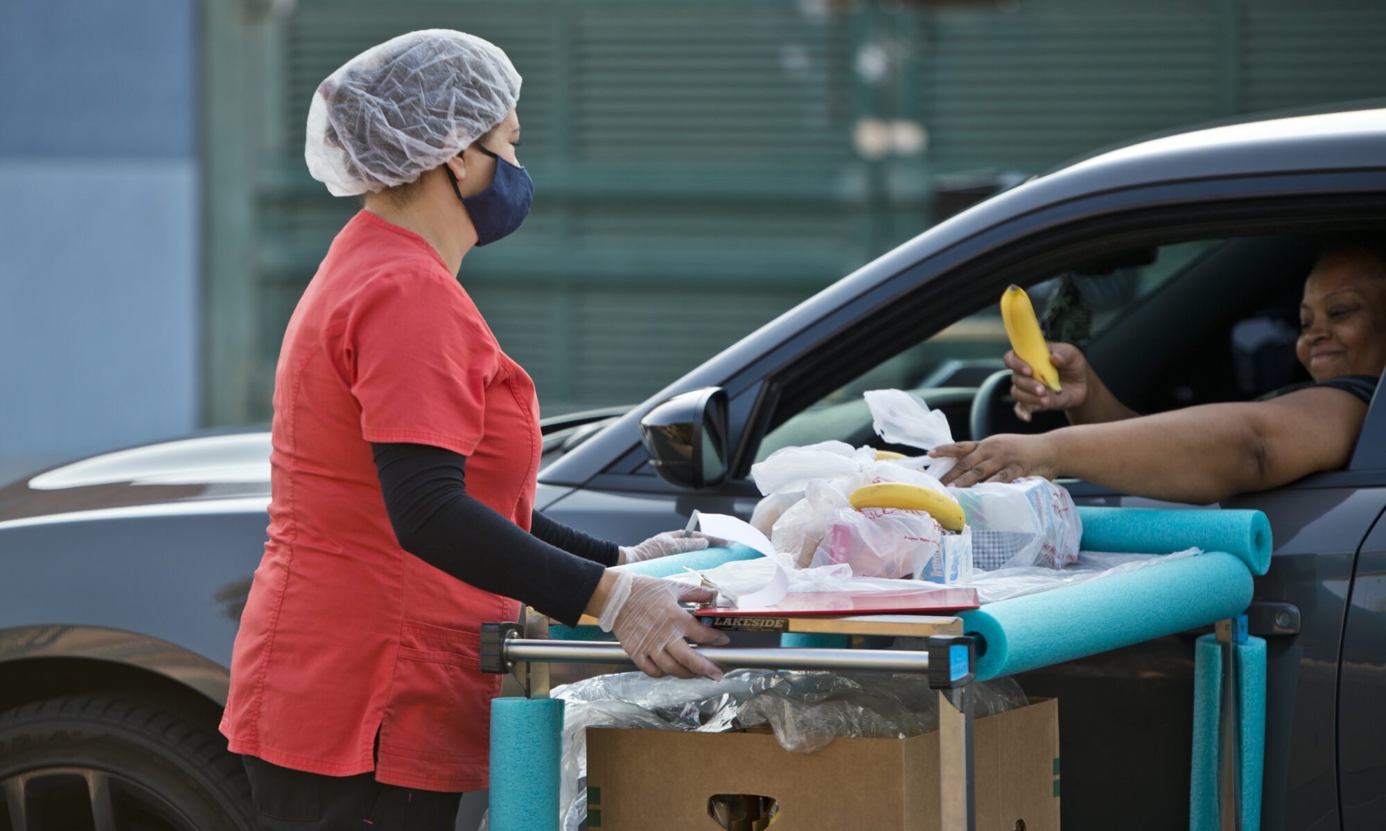 Una mujer recibe una bolsa de alimentos mediante la ventanilla de su carro.