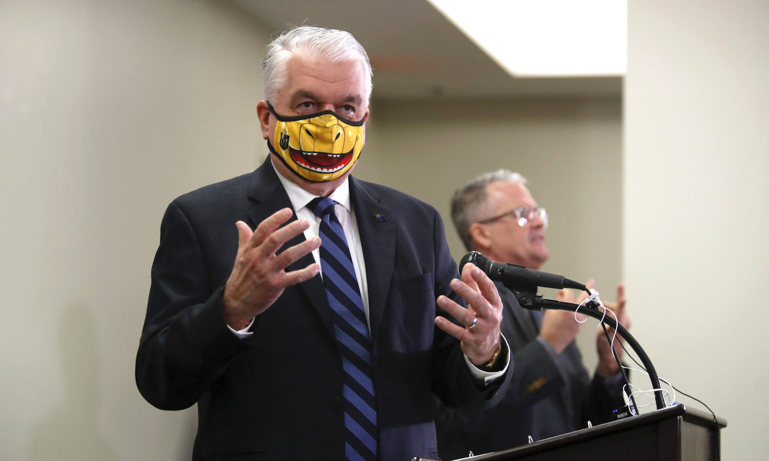 El gobernador de Nevada, Steve Sisolak, responde a una pregunta durante una conferencia de prensa. La mascarilla que porta tiene como tema a Chance the Golden Gila Monster, la mascota del equipo de hockey Vegas Golden Knights.