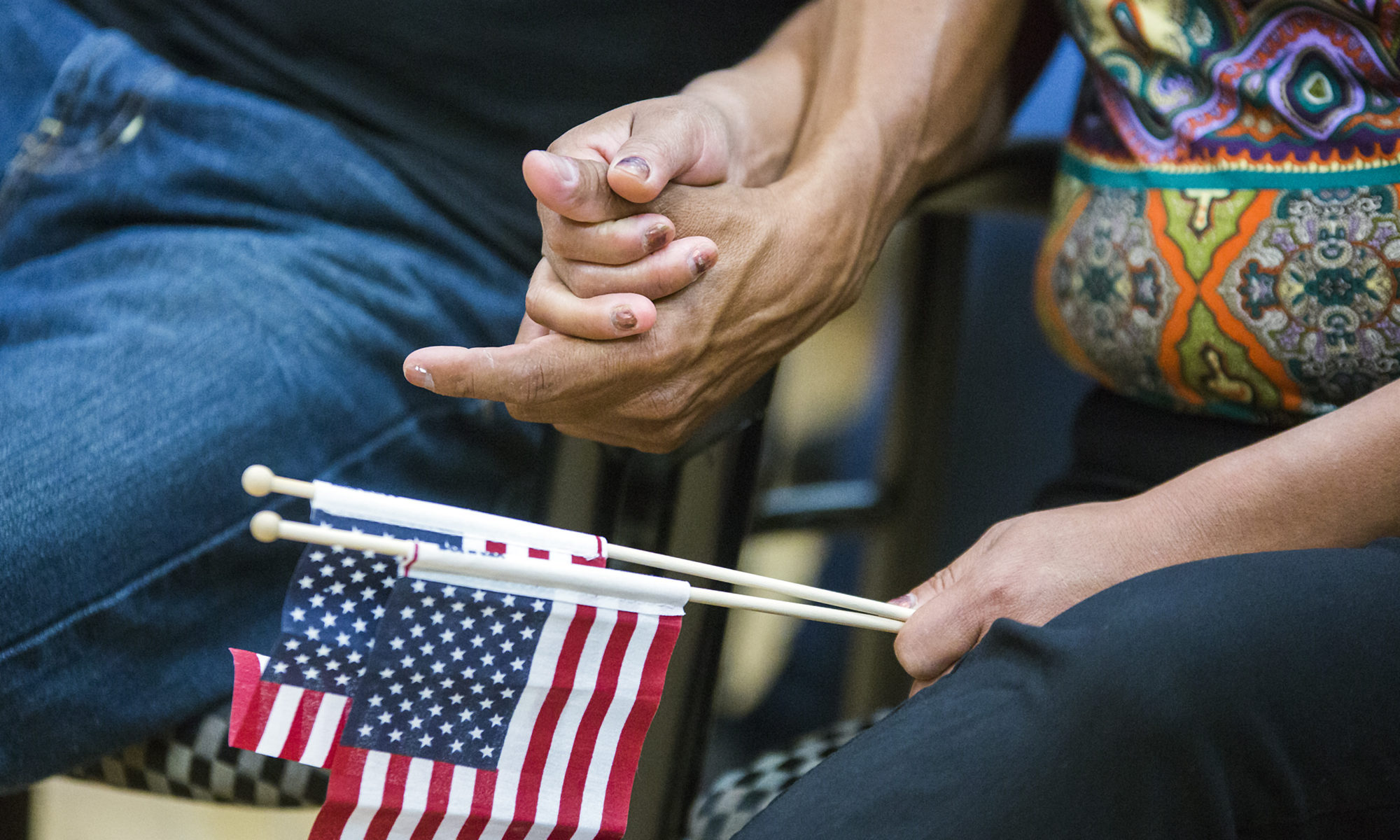 Dos personas tomándose de las manos con una bandera de los Estados Unidos