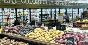 Una vista de fruta y verduras en una tienda. Palabras "Eat, Colorfully, Live Healthy"