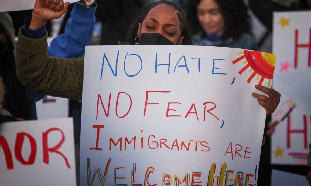 Mujer en una concentración contra la inmigración con un cartel en el que se lee «No al odio, no al miedo, los inmigrantes son bienvenidos aquí»