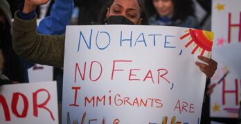 Mujer en una concentración contra la inmigración con un cartel en el que se lee «No al odio, no al miedo, los inmigrantes son bienvenidos aquí»