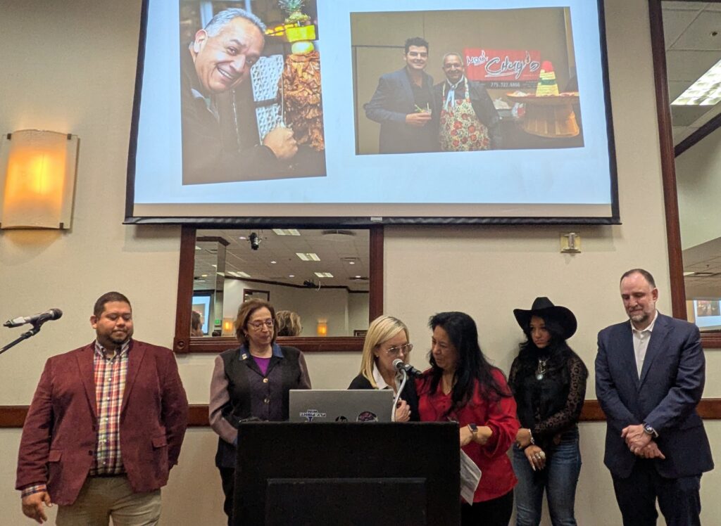 seis personas de pie en un podio frente a una pantalla de proyecto con fotos
