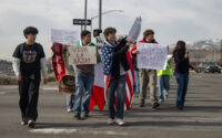 Un grupo de estudiantes caminando por un estacionamiento con diversos carteles en protesta contra el ICE.