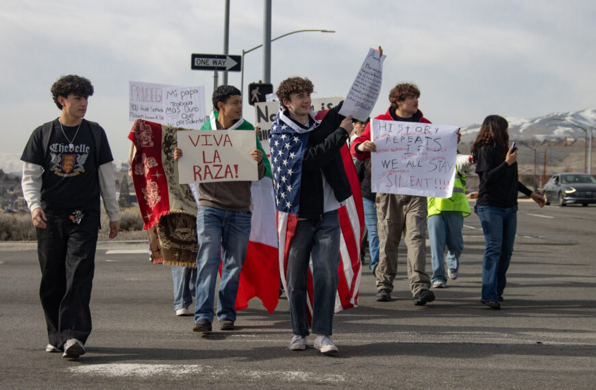 Un grupo de estudiantes caminando por un estacionamiento con diversos carteles en protesta contra el ICE.