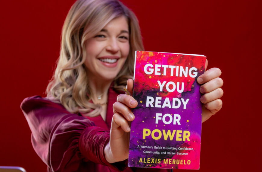 Una mujer rubia sentada en un escritorio sosteniendo un libro que dice: "Preparándote para el poder."